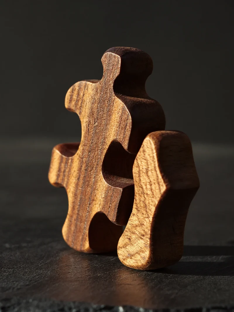 Holzpuzzle mit unregelmässig geschnittenen Teilen auf dunklem Schieferuntergrund bei Seitenlicht