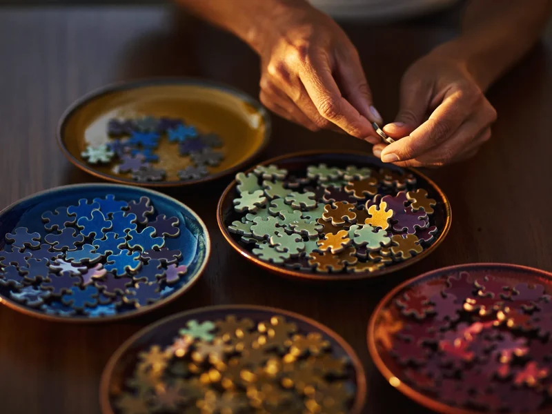 Nach Farben sortierte Puzzleteile in kleinen Keramikschalen auf einem Tisch